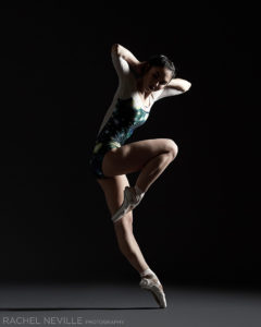 Dark ballet photo of Kyra Lin in a galaxy print leotard in a contemporary dance pose on pointe photographed by Rachel Neville