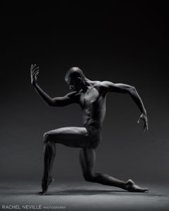 Muscular male dancer in dark lighting on one knee photographed by Rachel Neville